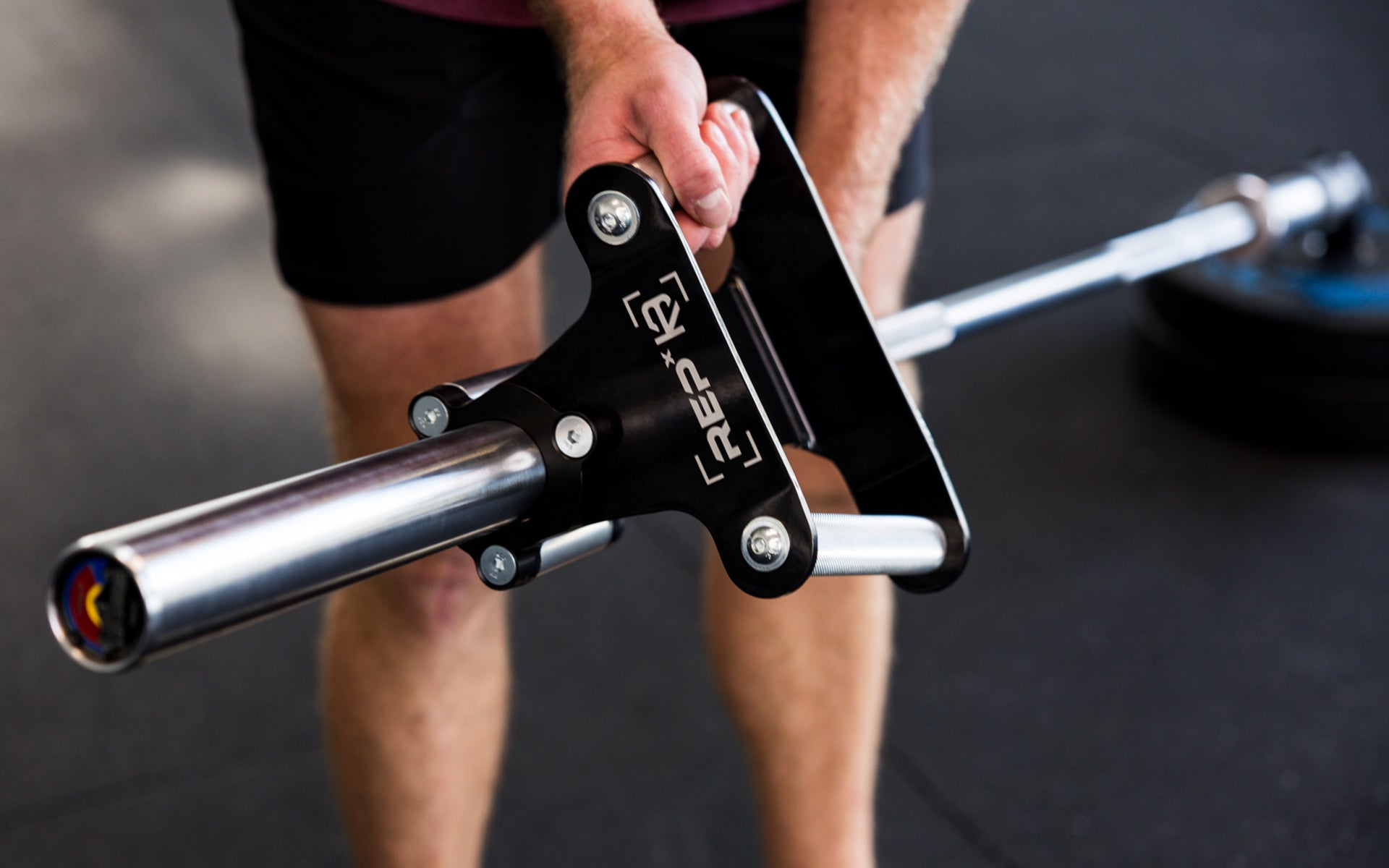 An athlete sliding a REP® x Kleva Built® Angled Atlas™ Close-Grip Cable and Landmine Attachment onto a barbell